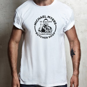 May include: White t-shirt with a black and white graphic of Michael Myers from the movie Halloween. The graphic is a circle with the text "Michael Myers" and "Butcher Shop" around the outside. The text "Est. 1978" and "Always Fresh" are also included in the graphic.