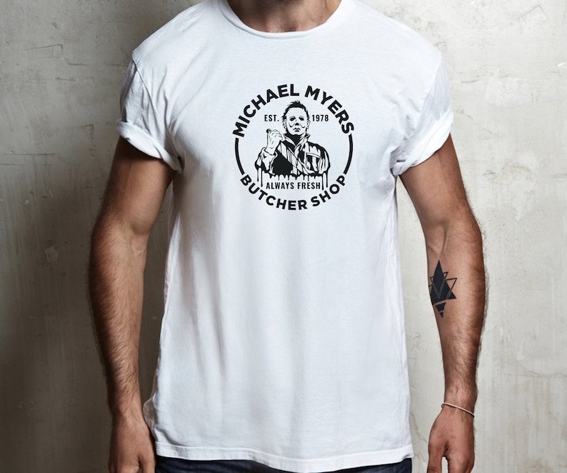 May include: White t-shirt with a black and white graphic of Michael Myers from the movie Halloween. The graphic is a circle with the text "Michael Myers" and "Butcher Shop" around the outside. The text "Est. 1978" and "Always Fresh" are also included in the graphic.