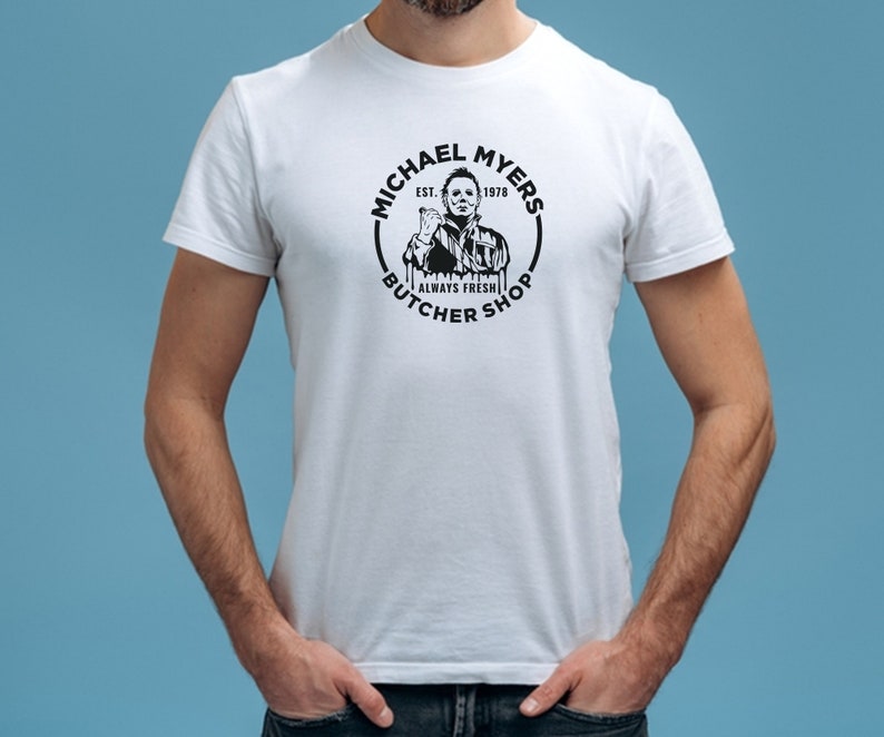 May include: White t-shirt with a black and white graphic of Michael Myers from the Halloween movies. The graphic includes the text "Michael Myers Butcher Shop Est. 1978 Always Fresh".
