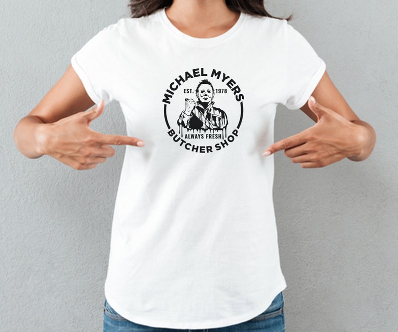 May include: White t-shirt with a black and white graphic of Michael Myers from the movie Halloween. The graphic is a circle with the text "Michael Myers Butcher Shop Est. 1978 Always Fresh" around the image of Michael Myers.