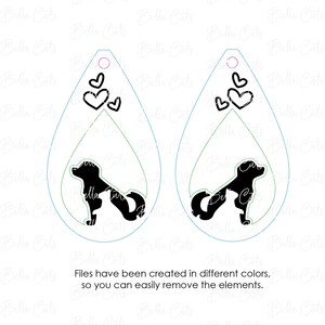 May include: A pair of white teardrop-shaped earrings with a black silhouette of a dog and three hearts. The earrings are layered with green and blue outlines.
