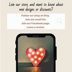 May include: A smartphone screen displaying a red heart-shaped light with glowing bulbs. The text on the screen reads: "Love our store, and want to know about new designs or discounts? Follow our shop on Etsy. Join our email list. Join our Facebook page. Leave a review."