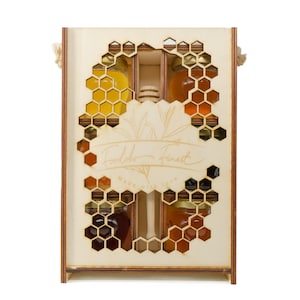 May include: Wooden gift box with a honeycomb design, containing several small glass jars of honey. The box has the text "Foodoko Finest" and "Made with love" etched on the front. The honey varies in color from light yellow to dark amber.