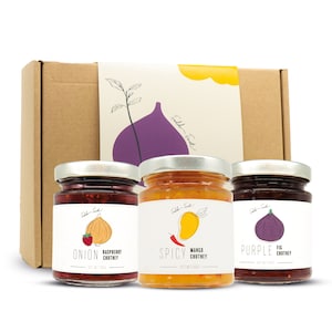 Può includere: Una confezione regalo contenente tre vasetti di chutney. I vasetti hanno coperchi argentati ed etichette bianche con illustrazioni di cipolla, mango e fico. Le etichette recitano "Onion Raspberry Chutney", "Spicy Mango Chutney" e "Purple Fig Chutney".