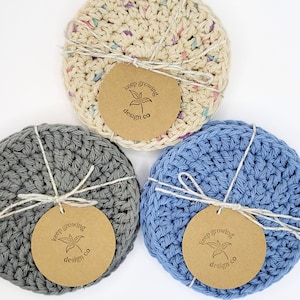 May include: Three crocheted coasters in gray, blue, and cream with a brown circle tag that says "keep growing design co" on each.