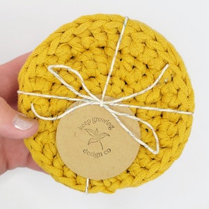 May include: Set of two yellow crocheted coasters with a brown paper tag that says "keep growing design co."