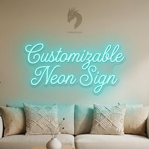 Op de afbeelding: Een turquoise neonbord met de tekst "Customizable Neon Sign" in een sierlijk lettertype. Het bord is bevestigd aan een neutrale muur boven een beige bank met kussens. De afbeelding bevat ook planten en een vaas met decoratieve stelen.
