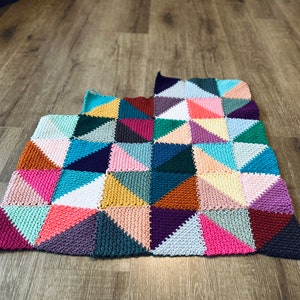 May include: A colorful crocheted blanket with a geometric pattern of triangles in shades of pink, blue, green, purple, orange, and brown.