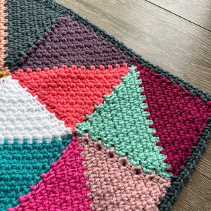 May include: A colorful crocheted blanket with a geometric pattern of triangles in shades of teal, pink, white, green, red, purple, and gray.