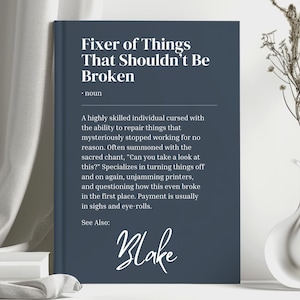May include: A dark blue book cover with the title "Fixer of Things That Shouldn't Be Broken" in white text. The book cover also includes the word "noun" and a description of a "highly skilled individual cursed with the ability to repair things that mysteriously stopped working for no reason." The book cover also includes the name "Blake" in cursive writing.