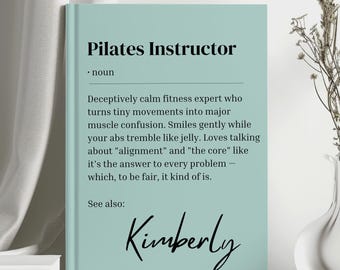 May include: A light teal Pilates Instructor definition print. The text includes a definition of a Pilates Instructor, with the name "Kimberly" in cursive at the bottom. The print is displayed next to a vase with dried flowers.