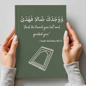Könnte beinhalten: Ein grünes Buch mit einer weißen Gebetsteppich-Illustration und einem arabischen Zitat, das übersetzt "Und Er fand dich verloren und führte dich." Das Zitat stammt aus dem Koran, Sure Ad-Duha (93:7).
