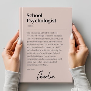 Puede incluir: Un libro rosa con el título "School Psychologist" y el texto "El GPS emocional del sistema escolar, que ayuda a los estudiantes a navegar por el estrés, la ansiedad y el caos general de la adolescencia. Tienen un suministro infinito de "Hablemos de eso" y "¿Cómo te sientes?" emparejado con la capacidad de identificar las señales sutiles de una crisis. Los psicólogos escolares brindan sabiduría, compasión y, ocasionalmente, una mirada de desaprobación ante el drama que de alguna manera nunca se detiene. Ver también: Charlie"