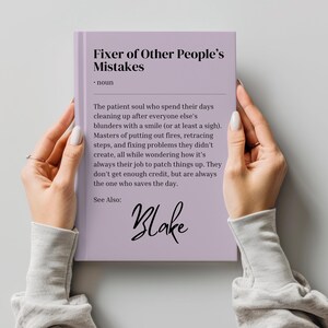 Könnte beinhalten: Ein lilafarbenes Buch mit dem Titel "Fixer of Other People's Mistakes" und einer Definition des Begriffs. Das Buch trägt eine handschriftliche Unterschrift mit dem Wort "Blake" am unteren Rand.