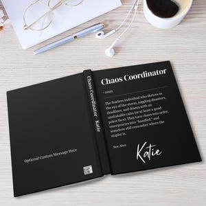 May include: Black and white book with the text "Chaos Coordinator - noun - The fearless individual who thrives in the eye of the storm, juggling disasters, deadlines, and drama with an unshakable calm (or at least a good poker face). They turn chaos into order, emergencies into 'handled,' and somehow still remember where the stapler is. See Also: Katie" on the cover. The book is open to reveal the text "Chaos Coordinator - Katie" on the left page and "Katie" on the right page.