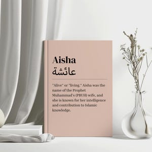 May include: A pink and white card with the name Aisha written in black. The Arabic word for Aisha is written in black below the name. The card also includes a definition of the name Aisha, which is "Alive" or "living." Aisha was the name of the Prophet Muhammad's (PBUH) wife, and she is known for her intelligence and contribution to Islamic knowledge.
