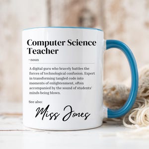 Peut inclure: Une tasse à café en céramique blanche avec un bord et une poignée bleus. La tasse présente une définition de "Professeur d'informatique" avec le nom "Miss Jones" en bas.