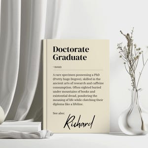以下が含まれることがあります： ベージュのカードに「Doctorate Graduate」というテキストと、その用語の定義が書かれています。定義は、博士号を取得し、研究とカフェイン摂取に精通した人物について説明しています。カードの下部には「Richard」という名前も記載されています。