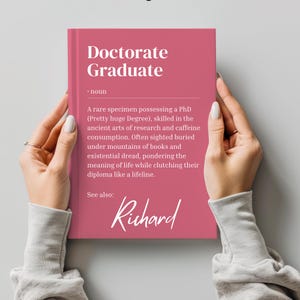 以下が含まれることがあります： 「Doctorate Graduate」というテキストと単語の定義が書かれたピンク色の本。定義には「Pretty huge Degree」というテキストが含まれています。本には「See also: Richard」というテキストも含まれています。