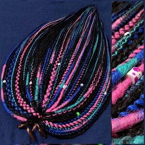 May include: A bundle of synthetic hair extensions in black, pink, blue, and teal colors. The hair is braided and tied together with a brown ribbon.