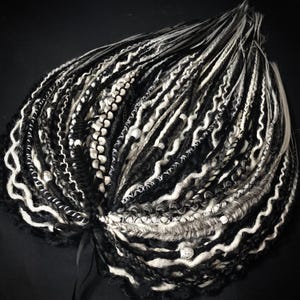May include: A bundle of black and white dreadlocks with various textures, including smooth, braided, and wavy sections. The dreadlocks are arranged in a circular pattern, with a black ribbon at the base. The color palette is primarily black and white, with some gray accents.