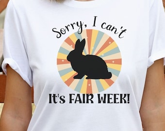 May include: White t-shirt with a retro-style graphic of a rabbit and the text "Sorry, I can't It's Fair Week!"