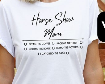 May include: White t-shirt with the text "Horse Show Mom" and a list of tasks: "Buying the coffee, Packing the tack, Holding the horse, Taking the pictures, Catching the sass."