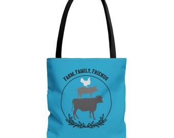 May include: A bright blue tote bag with black handles featuring a circular graphic of a cow, a pig, and a chicken stacked vertically. The text "FARM, FAMILY, FRIENDS" is printed in a black arc above the animals, framed by a thin black line and leaves.
