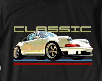 Puede incluir: Camiseta negra con un gráfico de un coche clásico blanco y la palabra "CLASSIC" encima. El coche tiene una franja azul y roja debajo. La palabra "PORSCHE" está impresa en el lateral del coche.