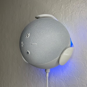 Peut inclure: Un haut-parleur intelligent blanc avec un anneau lumineux bleu autour de la base. Le haut-parleur est recouvert d'un tissu maillé et comporte des boutons pour le contrôle du volume et un interrupteur de désactivation du microphone.