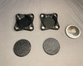 May include: Two black plastic square-shaped containers with a round, slightly raised center. Two black round discs with a textured surface. A white round disc with a silver center featuring the Apple logo.