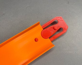 May include: A close-up of an orange plastic track piece with a red plastic connector. The connector has a circular opening and a series of ridges.