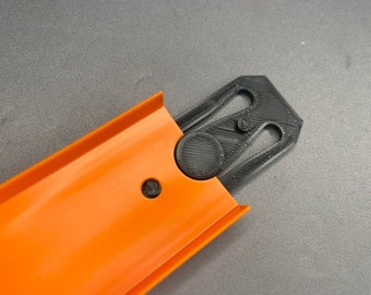 May include: Orange plastic track piece with a black plastic connector piece. The connector piece has a circular design with a small hole in the center.