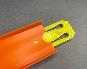 May include: A close-up of a yellow plastic track piece for a toy car racing set. The track piece has a circular connector on the left side and a slot on the right side. The track piece is designed to connect to other track pieces to create a race track.