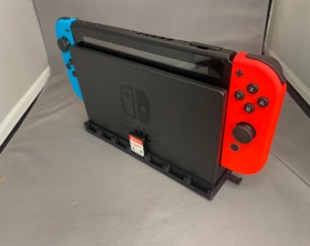 May include: A black Nintendo Switch console with a blue and red Joy-Con controller attached. The console is in a stand and has a game cartridge inserted.