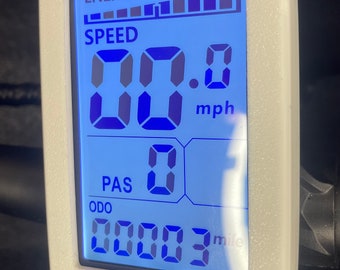 May include: A white digital display with a blue backlight shows the speed of 0.0 mph, the distance traveled of 0.03 miles, and a battery level indicator.