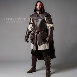 Op de afbeelding: Een persoon in een bruin leren middeleeuws kostuum, inclusief een capuchon, borstpantser, armbeschermers, handschoenen, een riem met zakjes en kniehoge laarzen. De tekst "LEATHER STUDIO - GENUINE LEATHER -" is zichtbaar. Het kostuum is van leer.