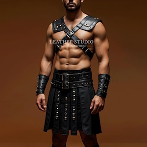 Op de afbeelding: Een man draagt een zwarte leren kilt met een gespikkeld riem en een zwart leren harnas met banden en gespen. Het harnas heeft een zilveren gesp met de tekst "LEATHER STUDIO" en "AGELESS IN LEATHER".