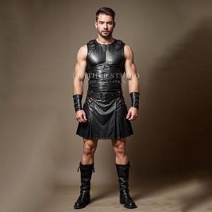 Pode incluir: Uma pessoa vestindo um colete de couro preto e uma saia escocesa combinando com uma fivela de cinto prateada. A pessoa está usando punhos de couro preto e botas de couro preto.