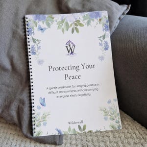 May include: A spiral-bound workbook titled Protecting Your Peace with a subtitle about staying positive in difficult environments. The cover features a white background with a watercolour floral border in shades of blue and green, a purple tree logo, and the brand name Wilderwell at the bottom.