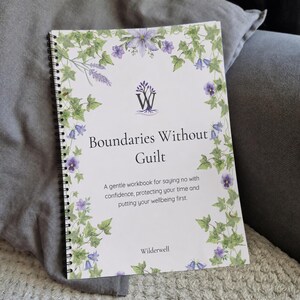 May include: A spiral-bound workbook titled Boundaries Without Guilt, featuring a white cover decorated with green ivy vines and purple flowers. The text reads Boundaries Without Guilt, A gentle workbook for saying no with confidence, protecting your time and putting your wellbeing first, and Wilderwell.
