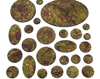 May include: A collection of circular and oval miniature bases featuring a textured, organic surface with green mossy patches, reddish-brown decay, clusters of small spherical growths, and embedded eye-like details across various sizes.