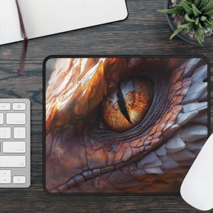 May include: A rectangular mousepad featuring a close-up of a dragon's eye. The eye is a vibrant orange and yellow, with a black slit pupil. The surrounding scales are shades of brown, orange, and white.