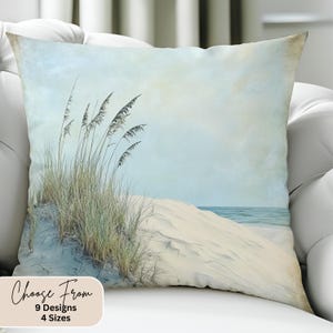 May include: A throw pillow with a beach scene featuring a sandy dune with tall grass and a blue ocean in the background. The pillow has a light blue and white background with a vintage, faded look. The text "Choose From 9 Designs 4 Sizes" is printed on the bottom of the pillow.