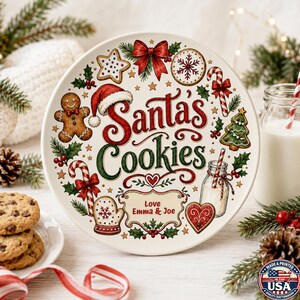 May include: A round white ceramic plate featuring the red and green text Santa's Cookies, surrounded by illustrations of a gingerbread person, candy canes, a Christmas tree, a snowflake, a mitten, a heart, and a label reading Love Emma & Joe.