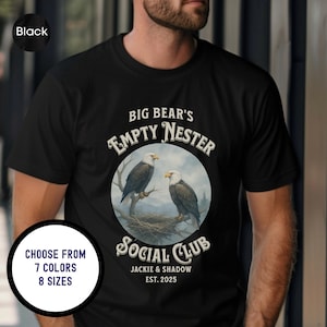 May include: Black t-shirt with a circular graphic featuring two eagles perched on a branch, with a nest in the background. The text reads "BIG BEAR'S EMPTY NESTER SOCIAL CLUB" with "JACKIE & SHADOW EST. 2025" below. The shirt is available in 7 colors and 8 sizes.