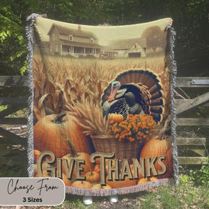 May include: A woven throw blanket with a Thanksgiving theme. The blanket features a turkey, pumpkins, corn stalks, and the words "Give Thanks".