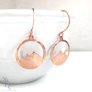 May include: A pair of copper earrings with a hammered finish. Each earring features a circle with a mountain silhouette cut out.