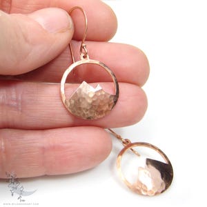 May include: A pair of rose gold earrings with a hammered circle design and a mountain silhouette cutout.