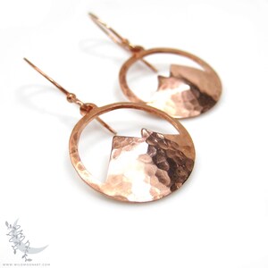 May include: A pair of copper earrings with a hammered texture. Each earring features a circular design with a mountain silhouette cut out.